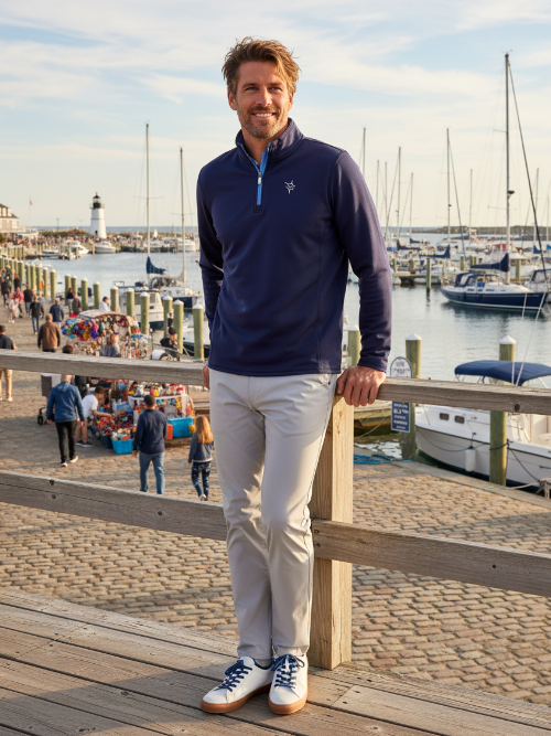 Man standing on a dock by a marina wearing a navy blue pullover with a logo.