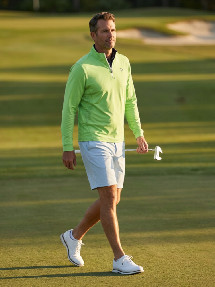 Man in a green jacket and white shorts walking on a golf course