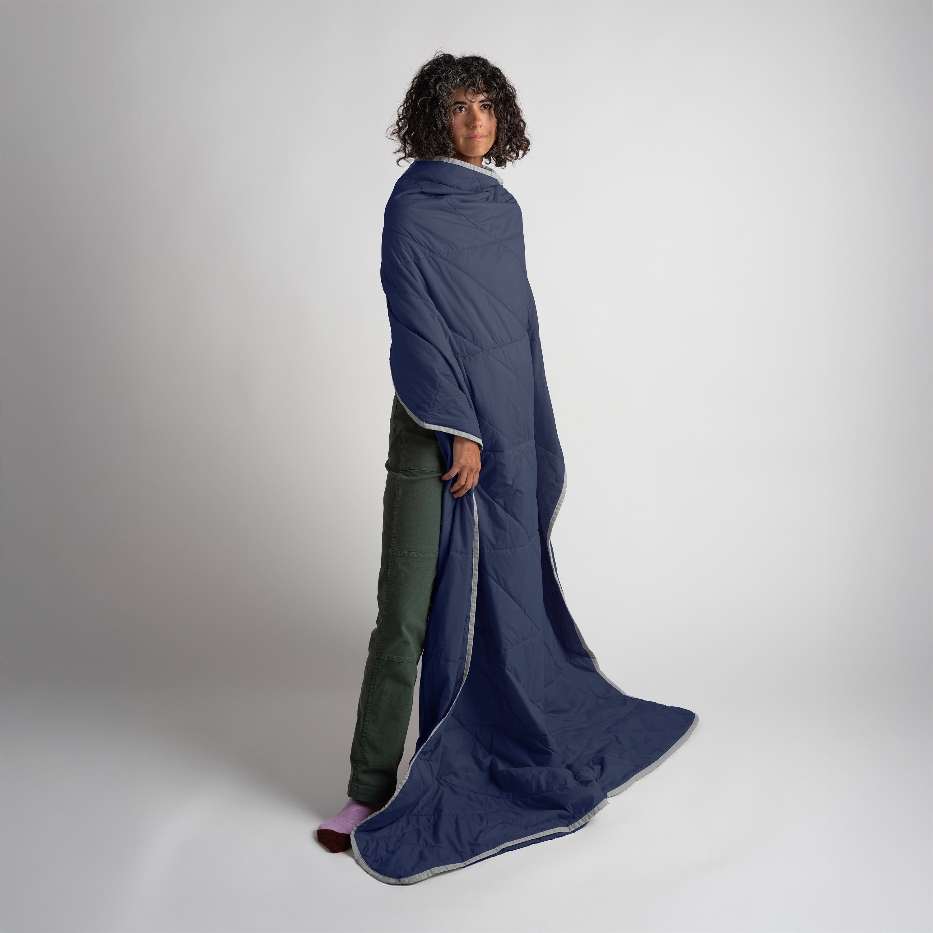 Person wearing a long navy blue blanket over their shoulders on a white background