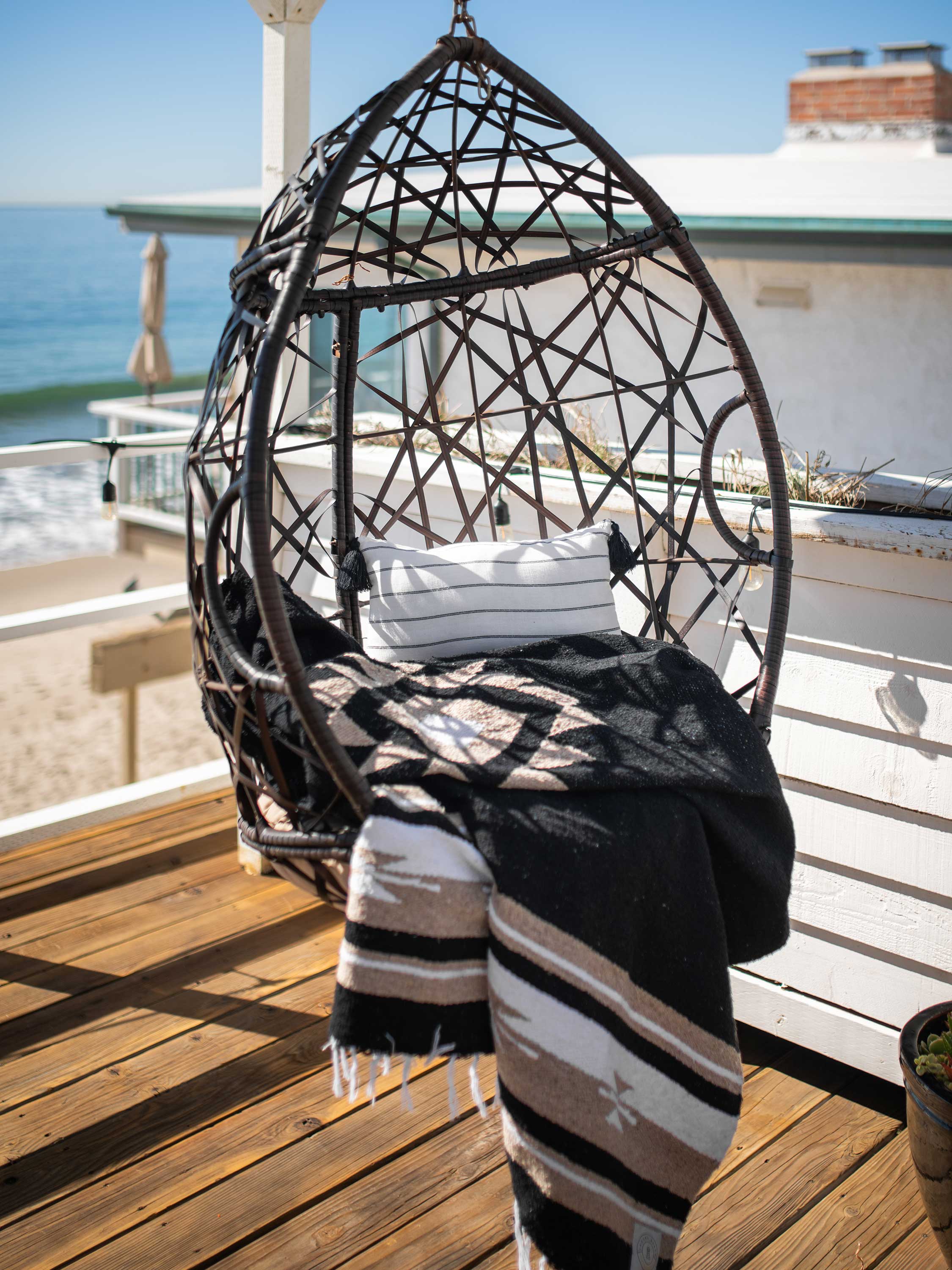 Hanging chair with a blanket and pillow on a wooden deck with ocean view