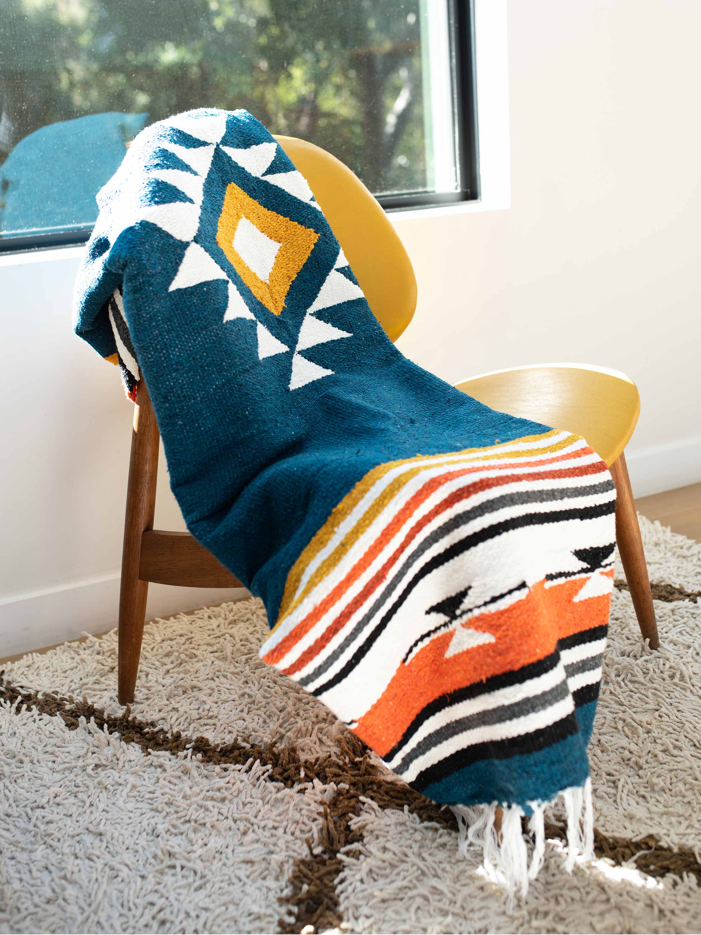 Colorful patterned blanket draped over a chair in a room with a window.