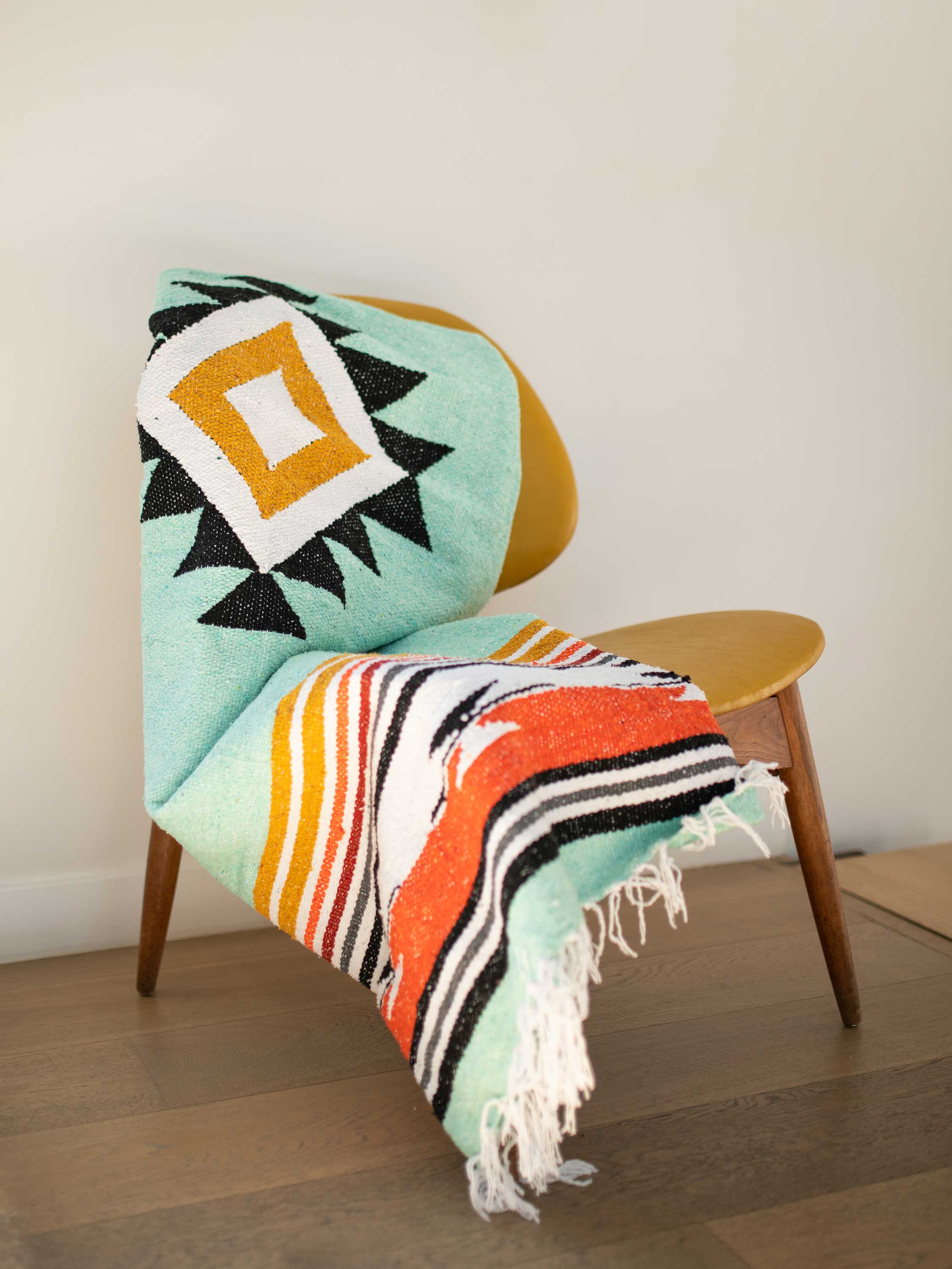 Colorful patterned blanket draped over a chair with a wooden floor and wall in the background