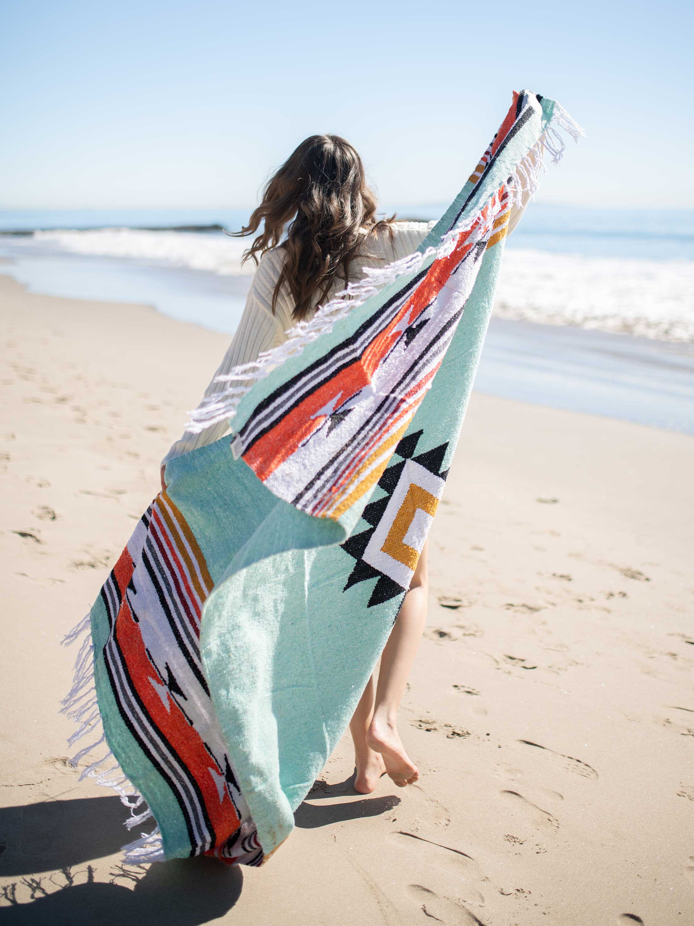 Person holding a colorful beach towel on a sandy beach with ocean waves in the background