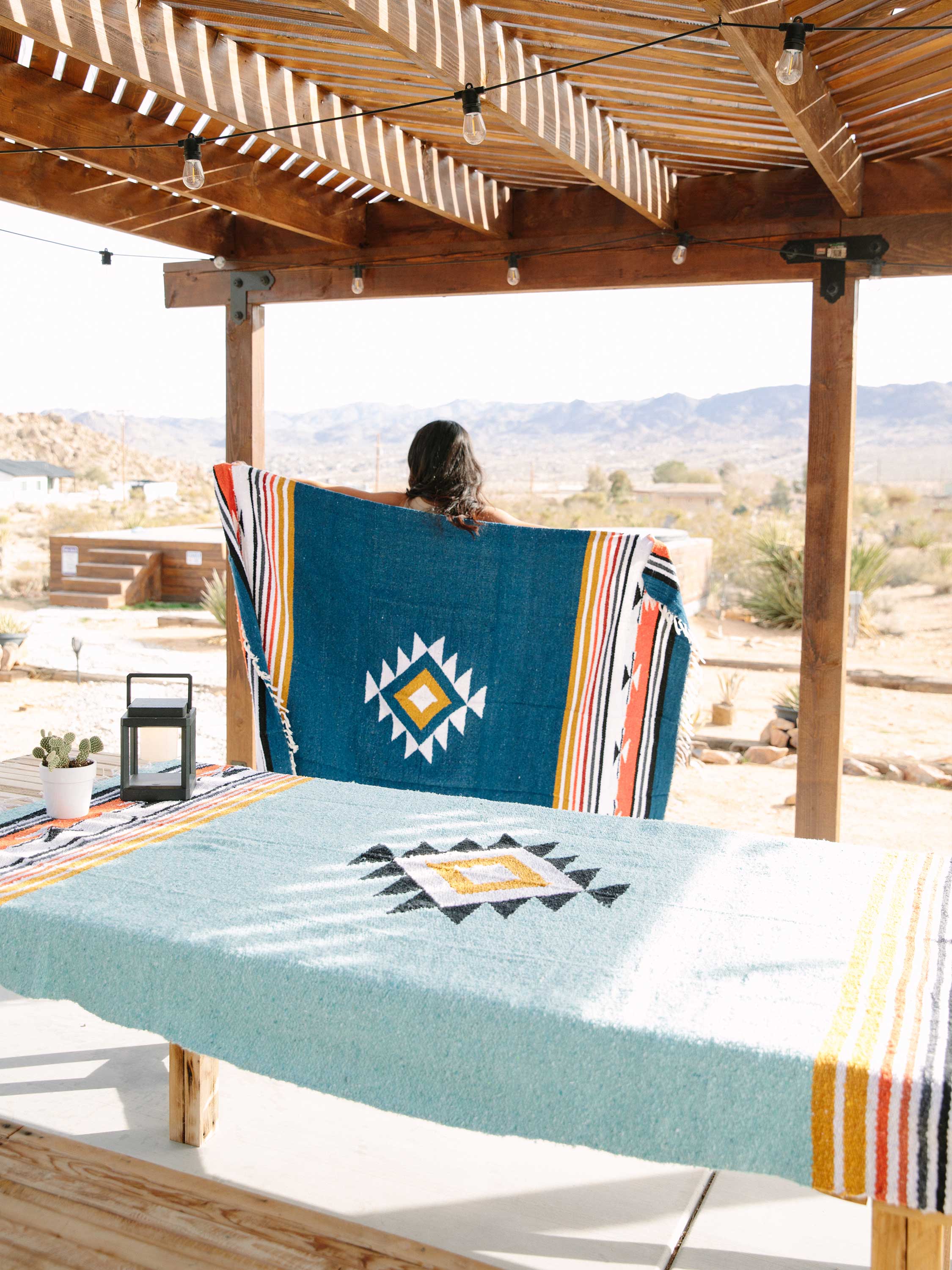 Person sitting on a wooden bench with a colorful blanket, overlooking a desert landscape.