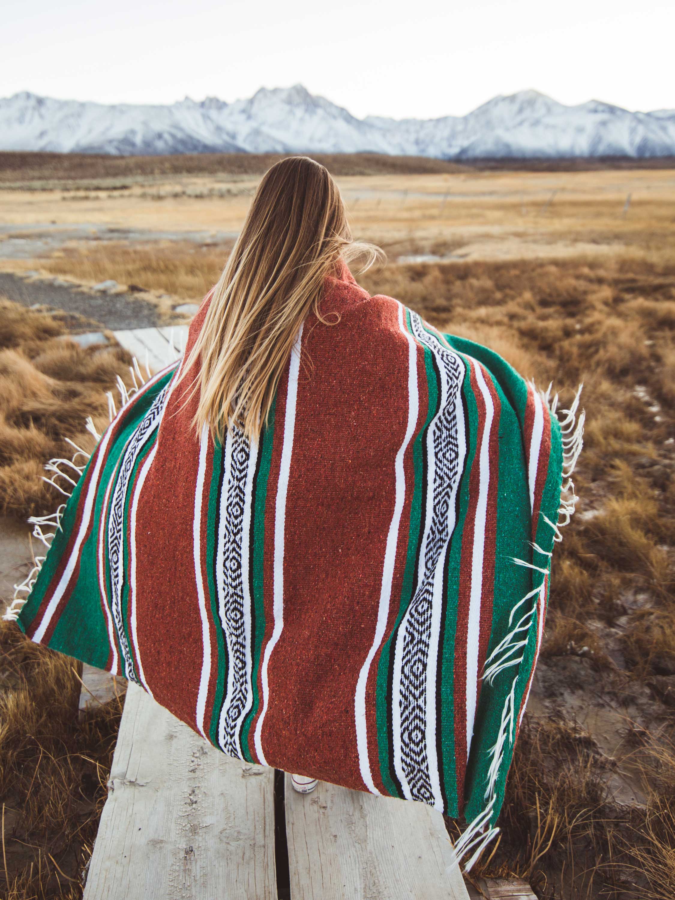 Person wrapped in a red, green, and white patterned blanket with mountains in the background