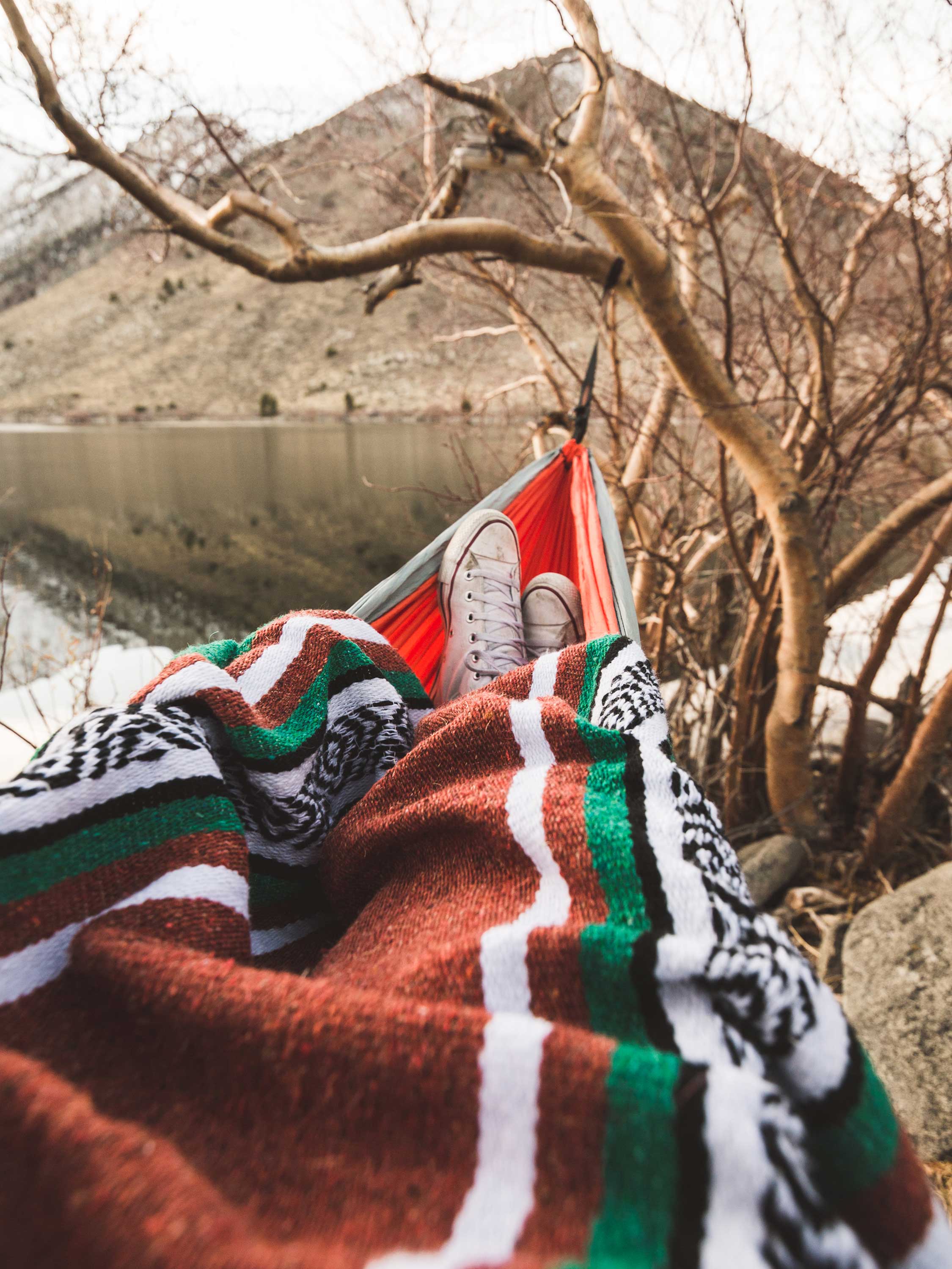 Person lying in a hammock with a colorful blanket, surrounded by nature.