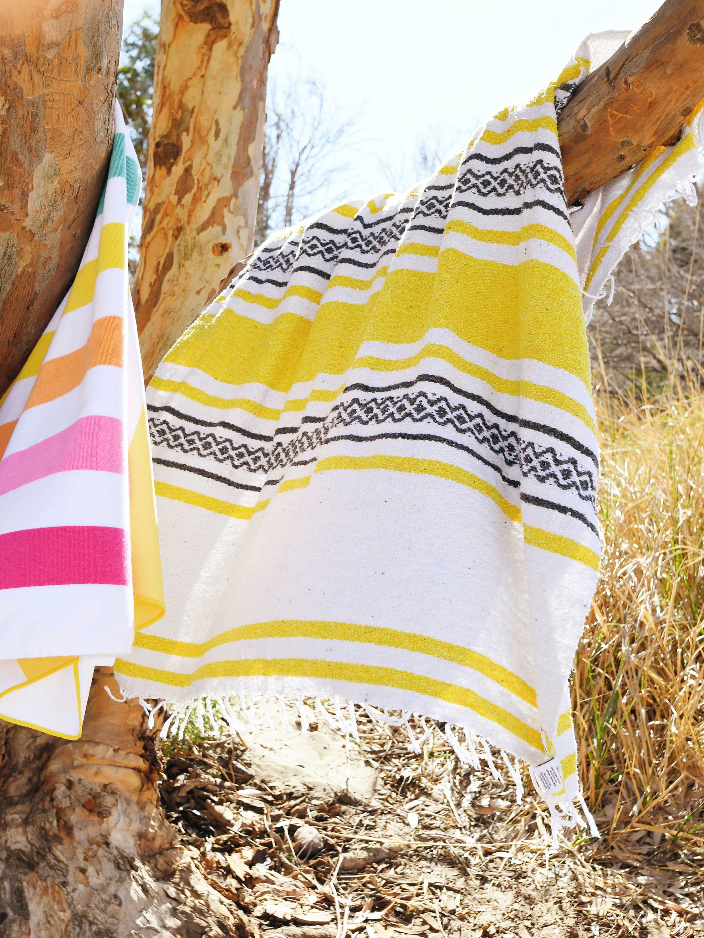 Yellow and white striped towel with geometric pattern draped over a wooden post outdoors.