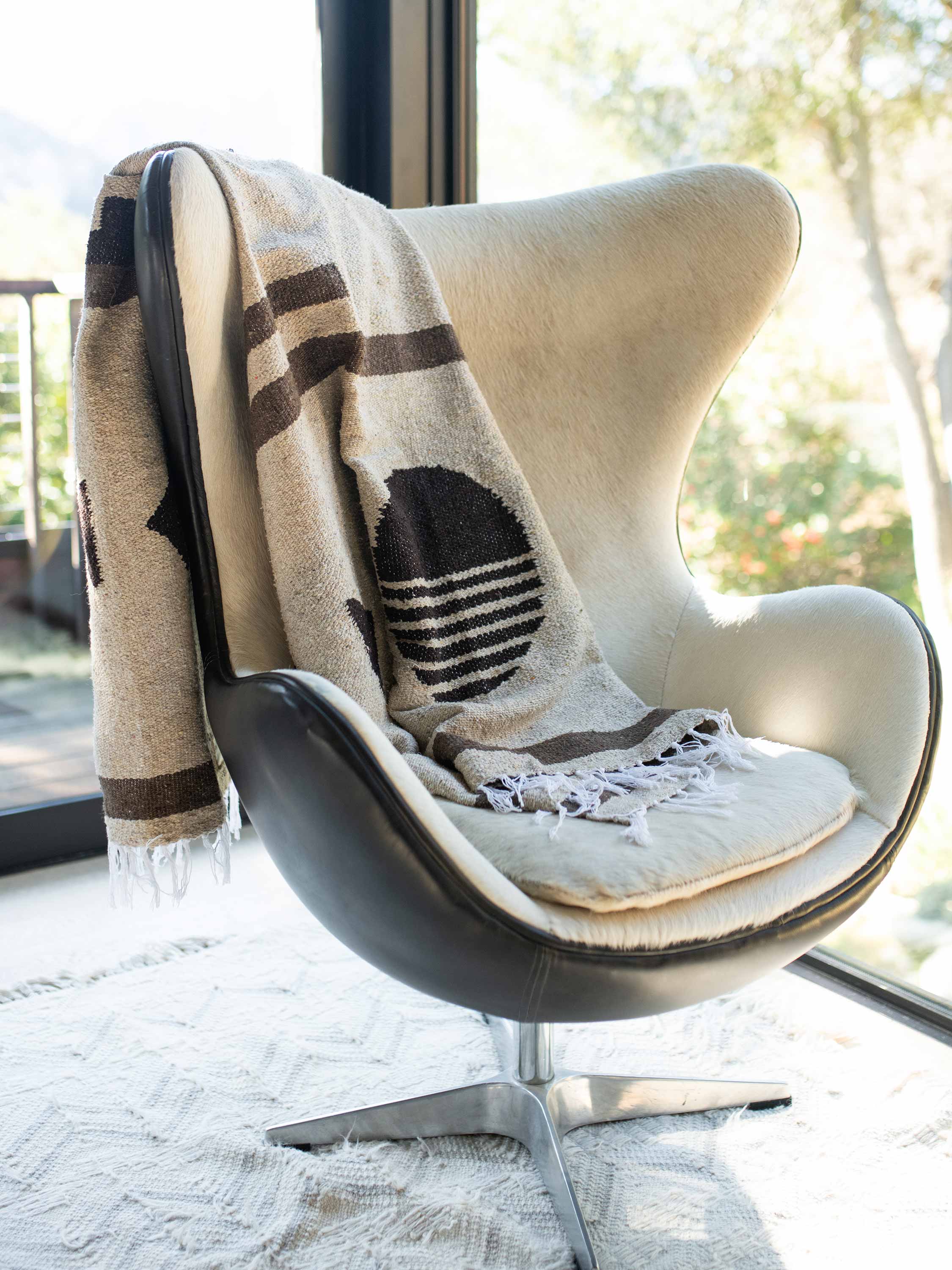 Modern chair with a patterned blanket draped over it, in a bright room with large windows.