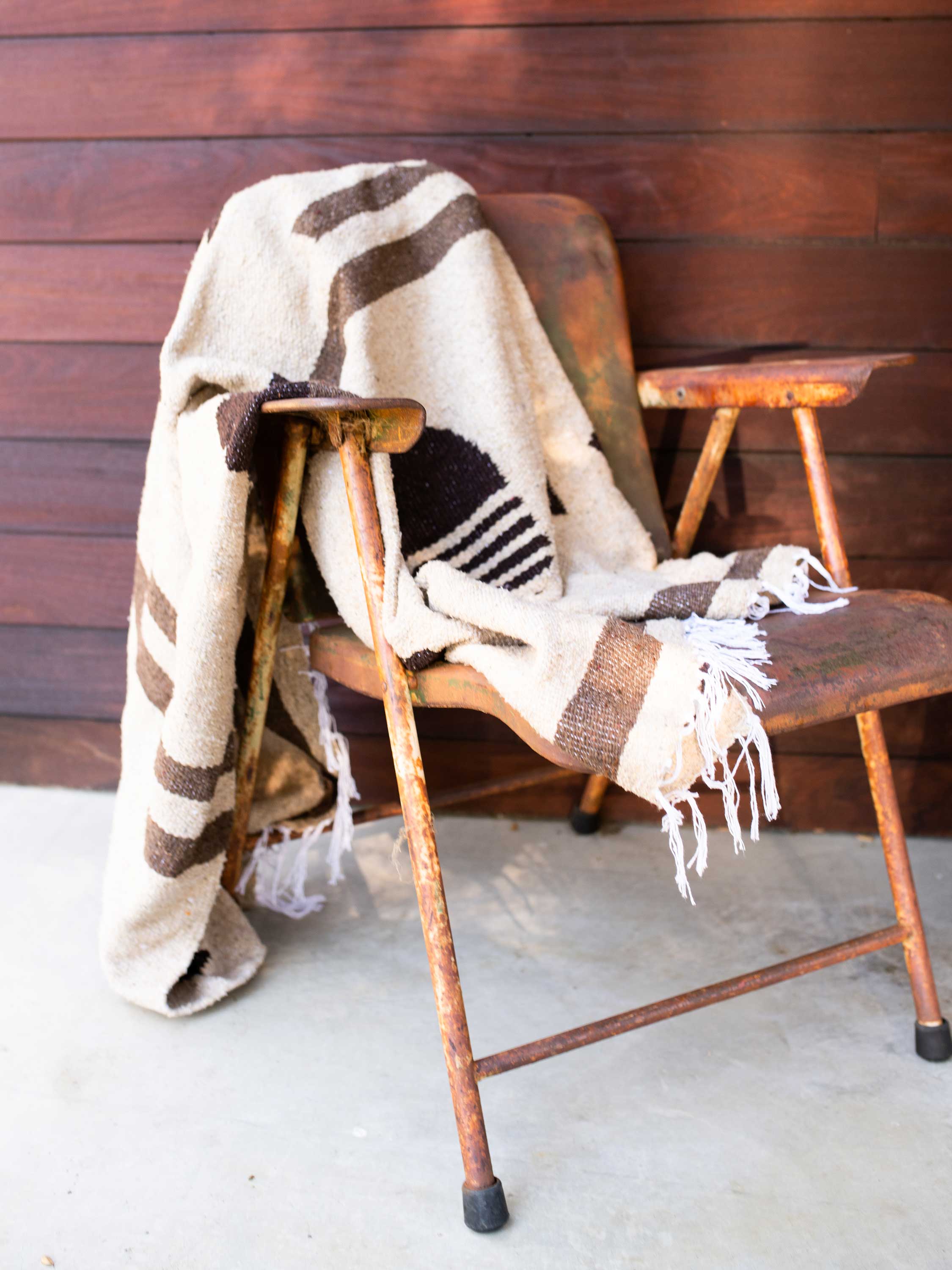 Plaid blanket draped over a wooden chair against a wooden wall.