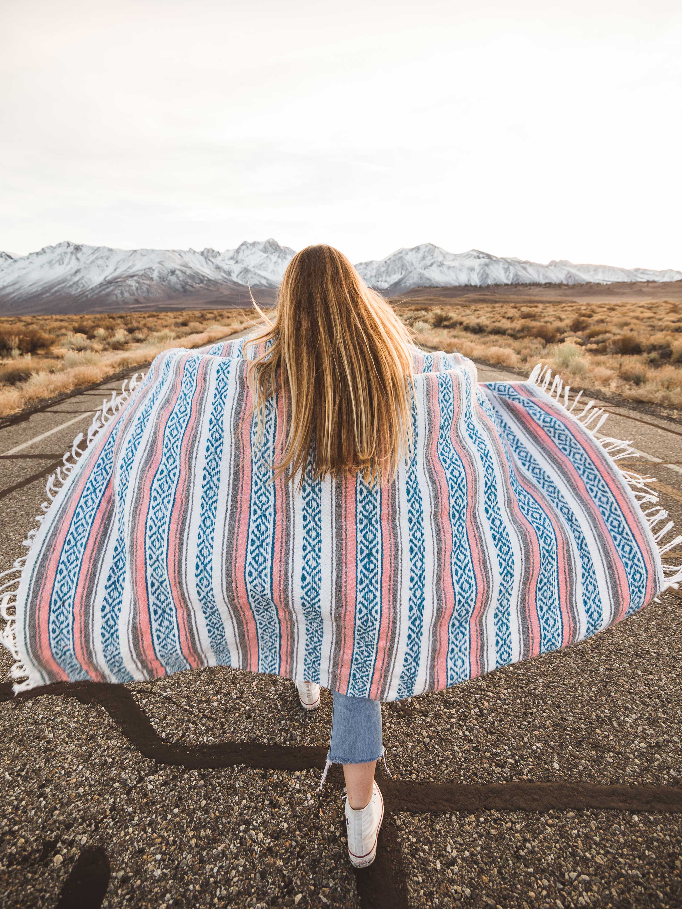 Person with a colorful patterned blanket in a desert landscape with mountains.