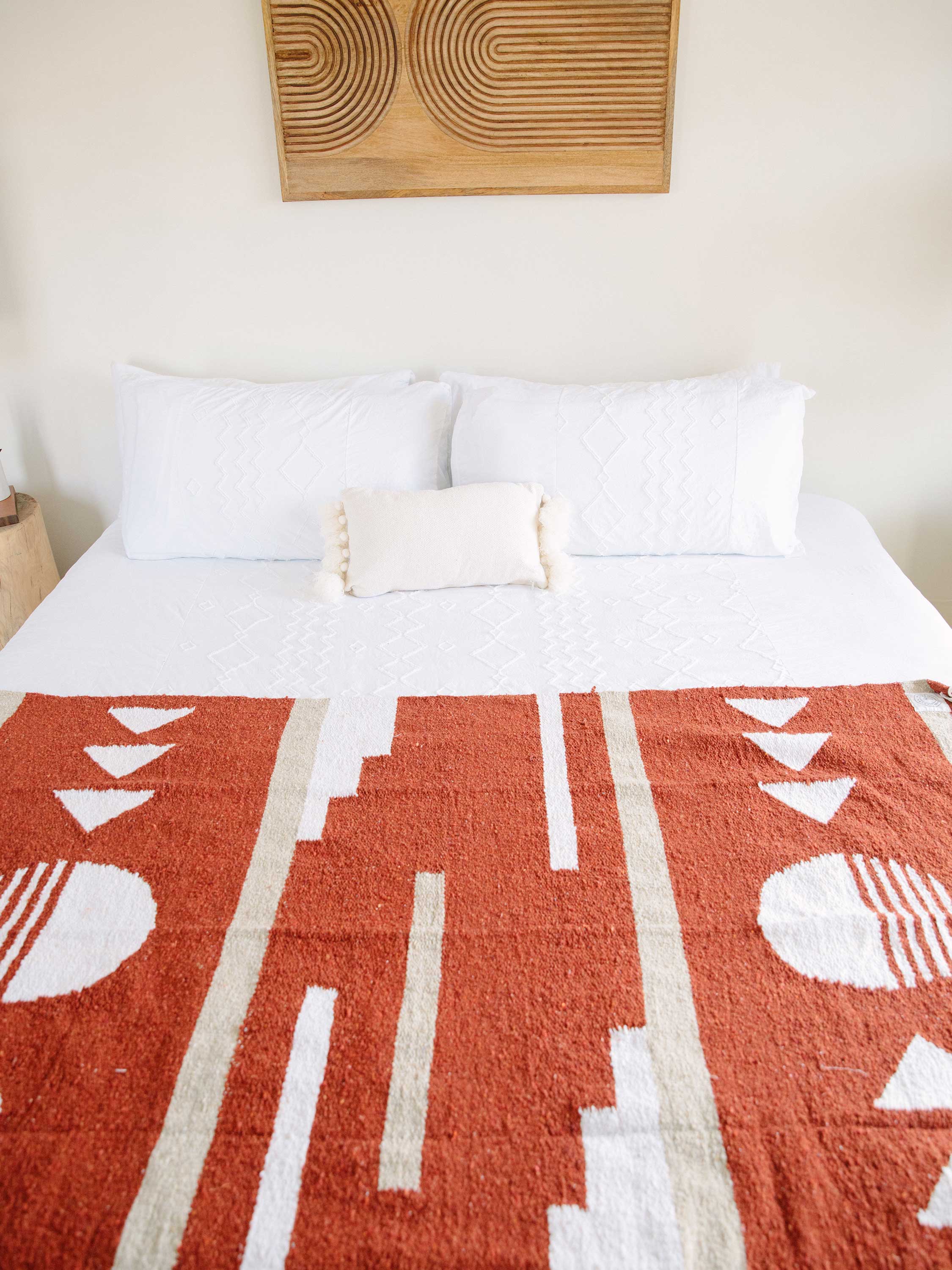 Bed with a red and white patterned blanket and wooden headboard.