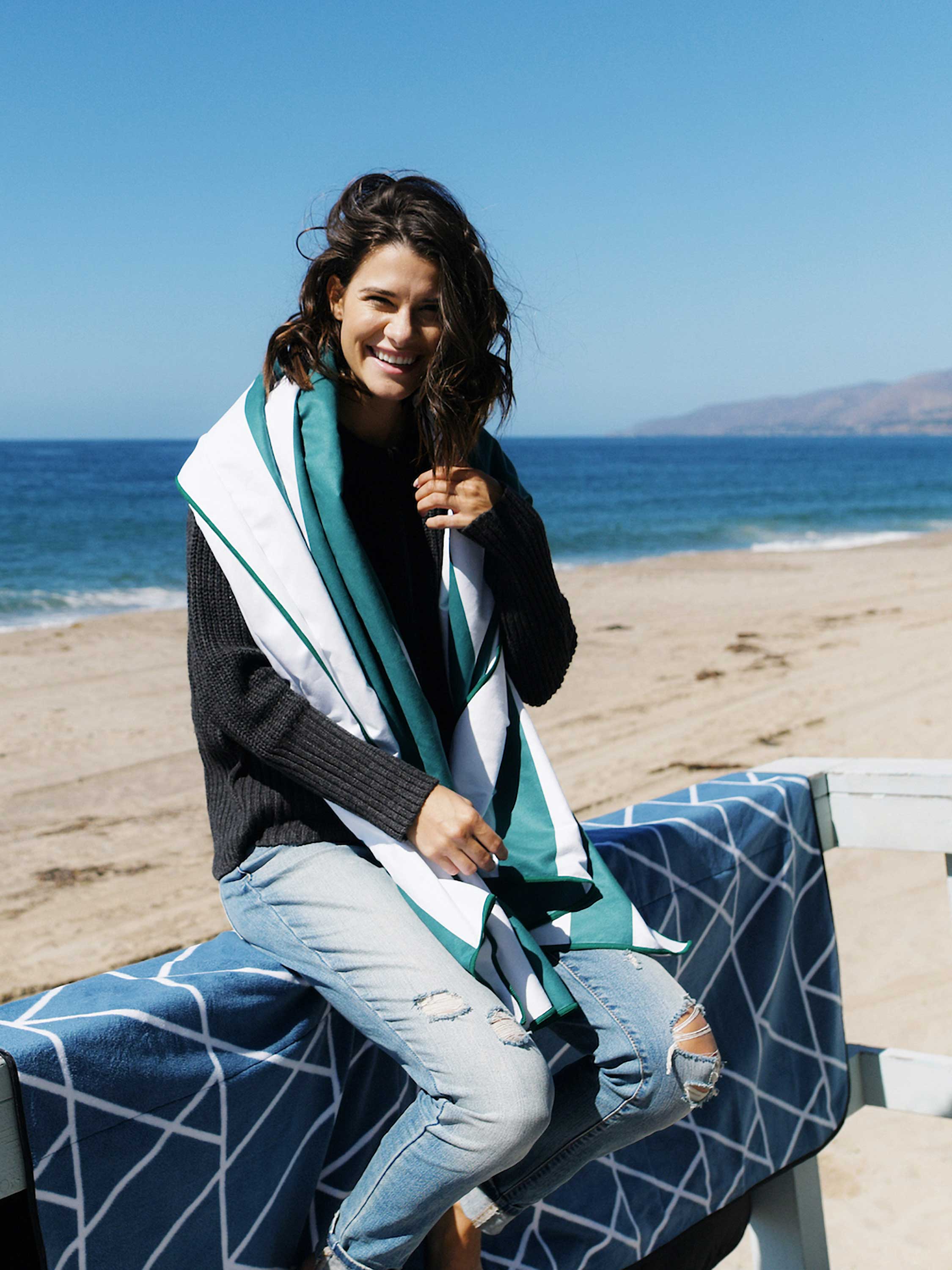 Woman sitting on a bench by the beach with a blue and white patterned blanket