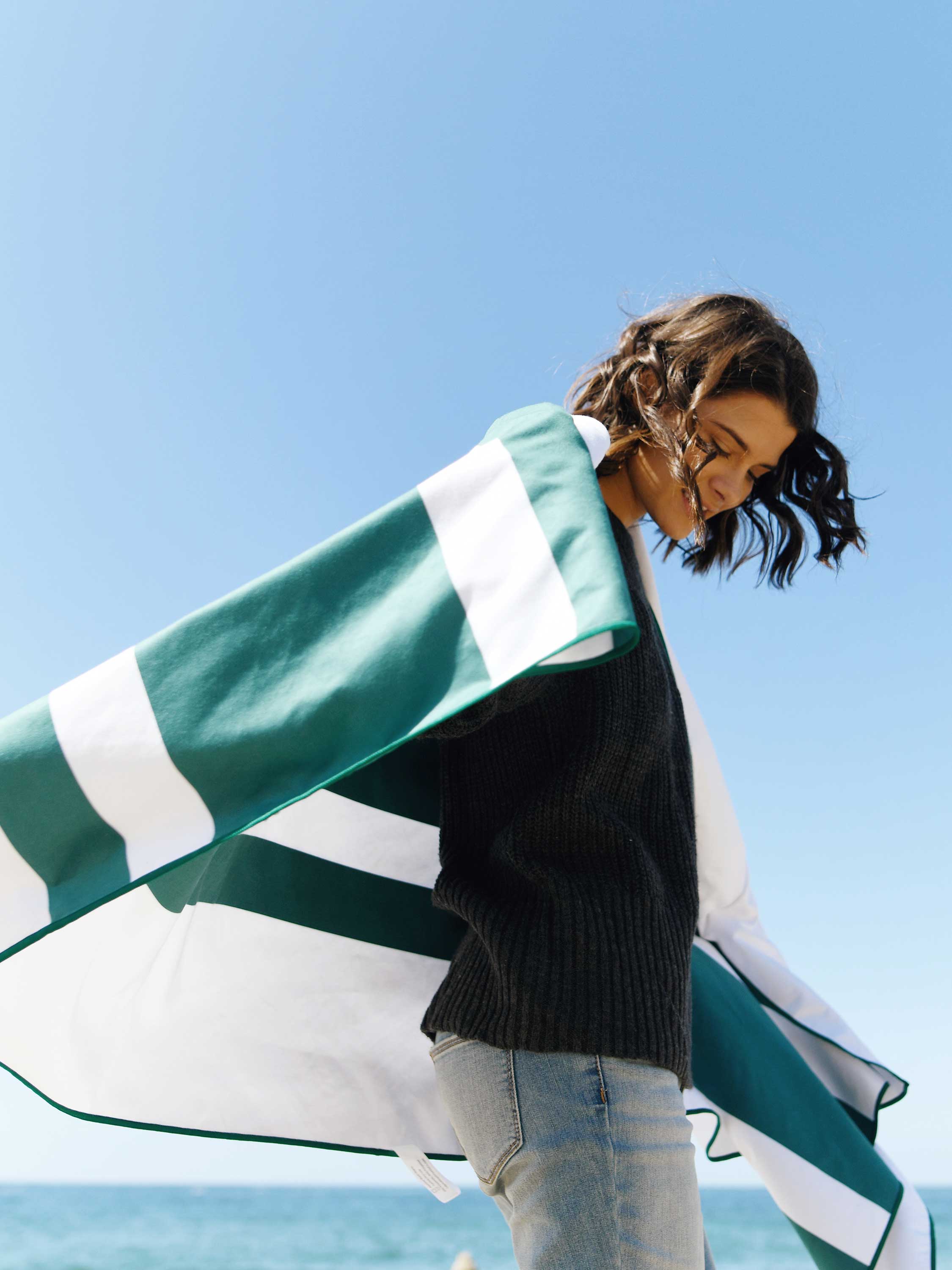 Woman holding a green and white striped towel against a clear blue sky