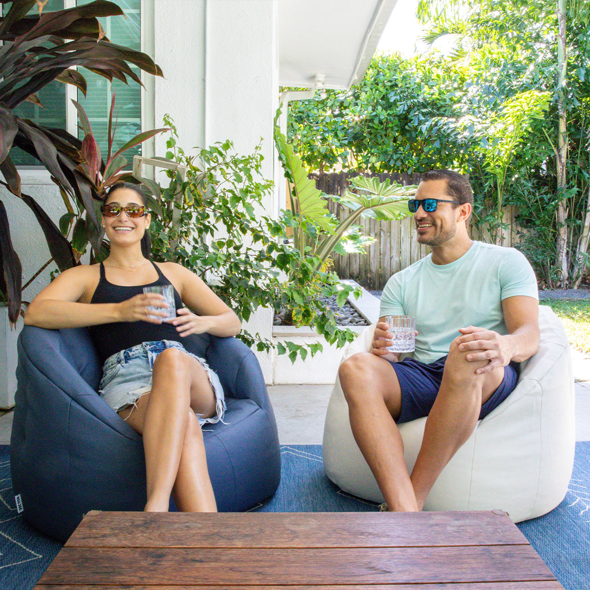 Two people sitting on bean bags outdoors with plants and a table in the background