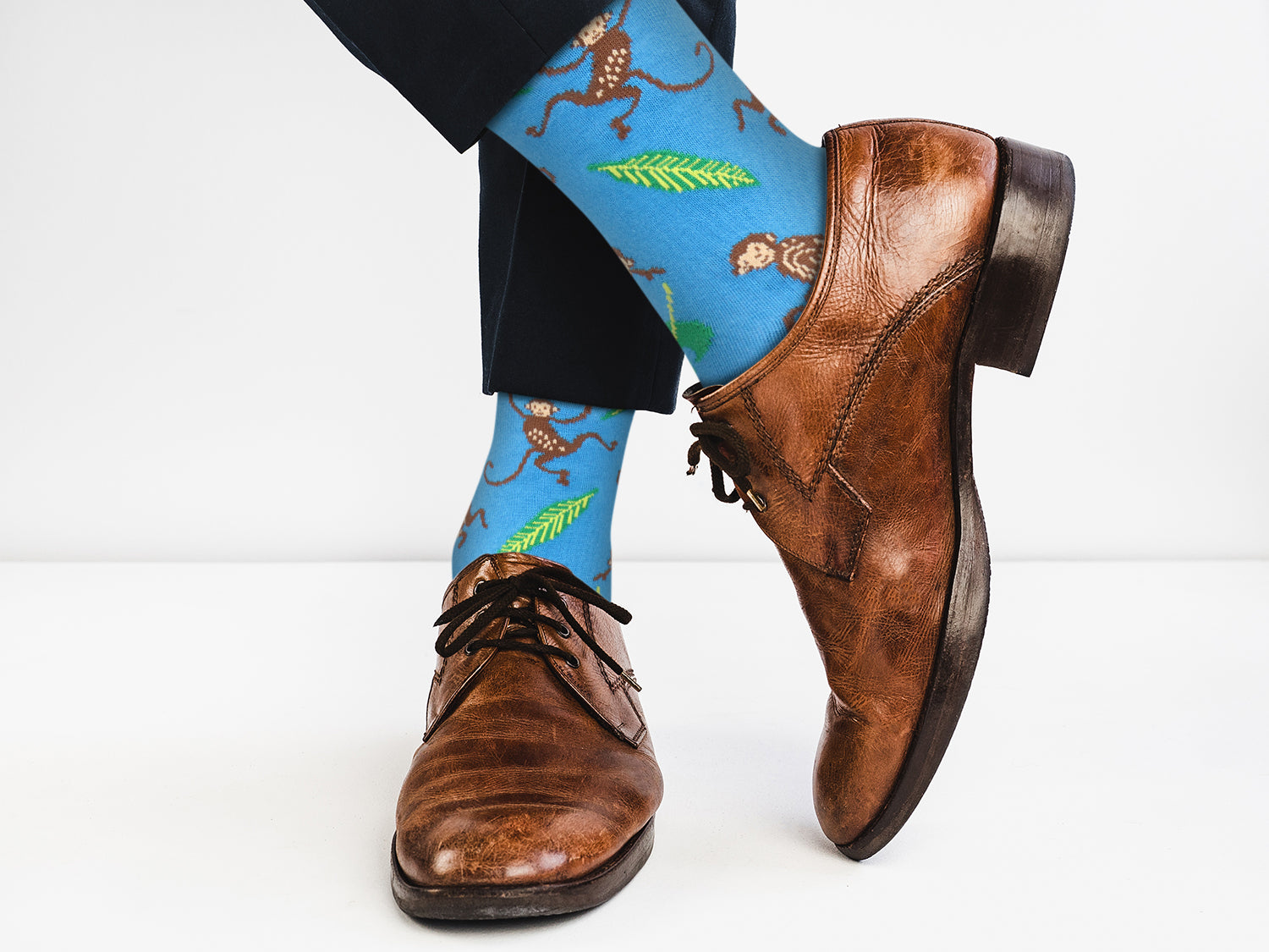 Blue socks with monkey and leaf pattern worn with brown dress shoes on a white background