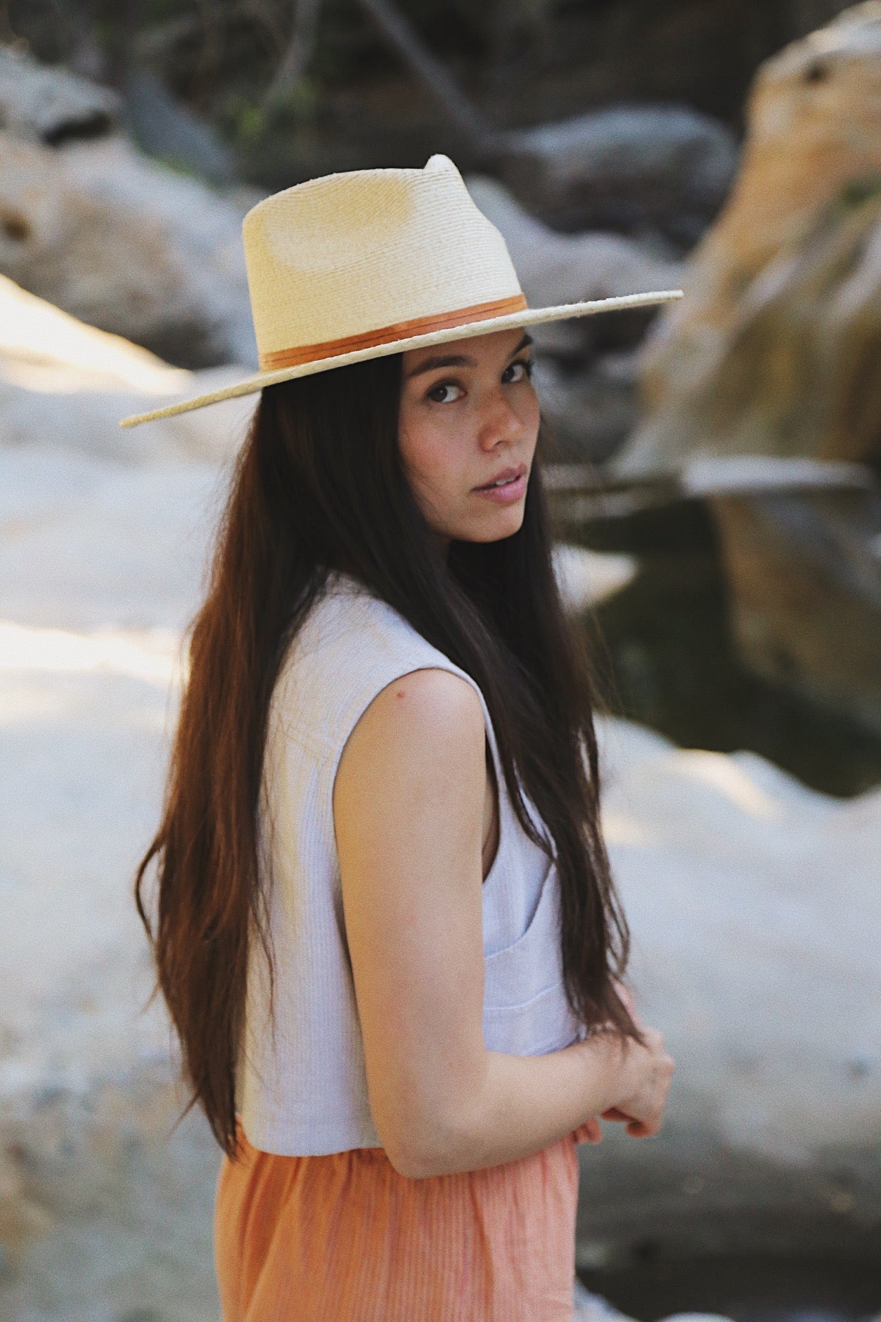 Woman wearing a wide-brimmed hat in a natural setting with rocks and water.