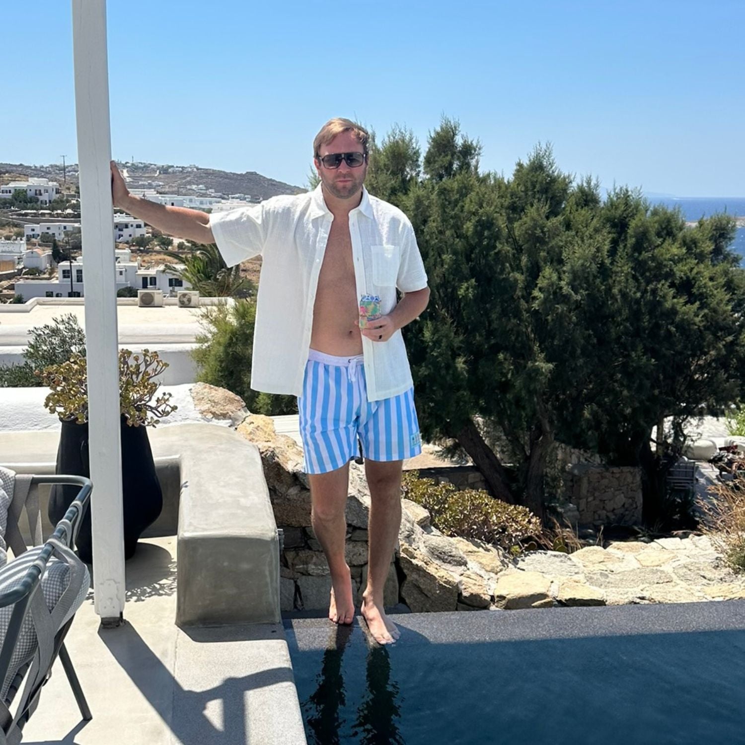 Man in striped swim shorts standing by a pool with a scenic background