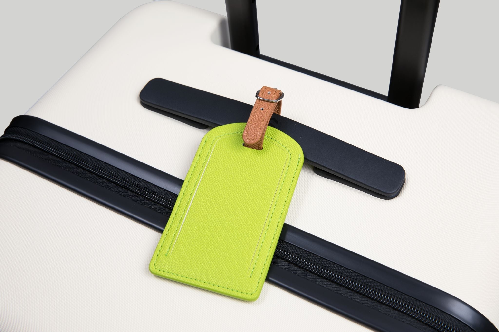 Green luggage tag attached to a black suitcase handle on a white surface.