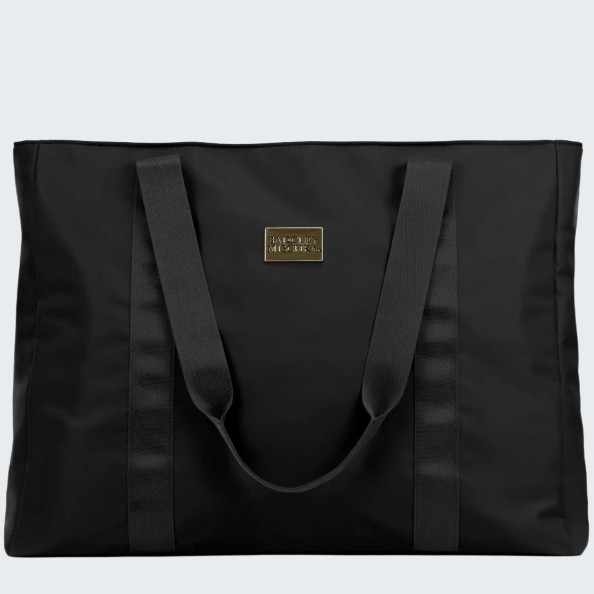 A black nylon tote bag with a shiny gold logo plate, soft webbing straps, and a zippered rear pocket. The bag is displayed in a way that showcases its spacious design and sleek finish.