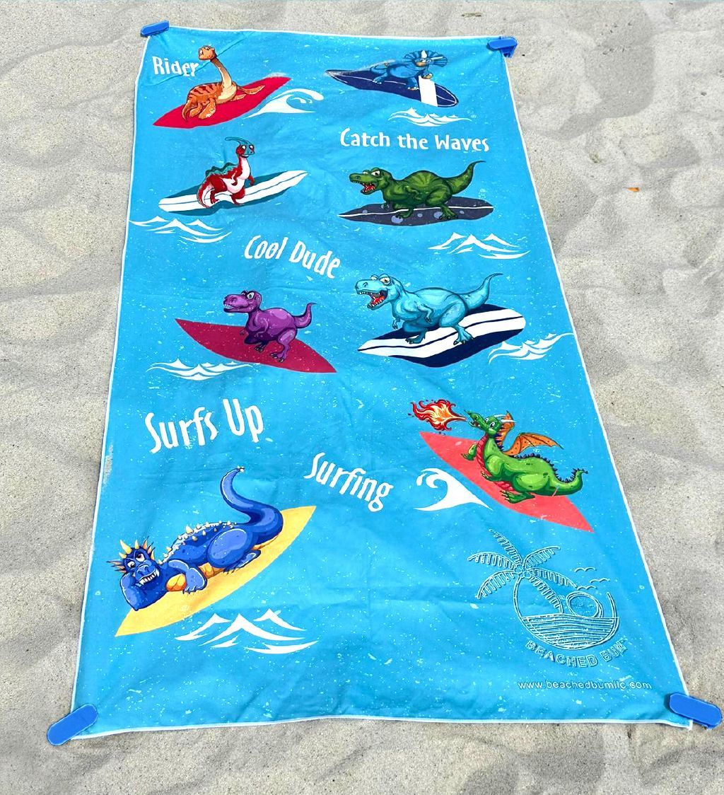 Blue beach towel with dinosaur graphics on a sandy background