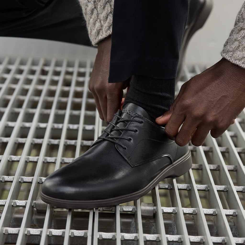 Person tying black leather shoes on a metal grate