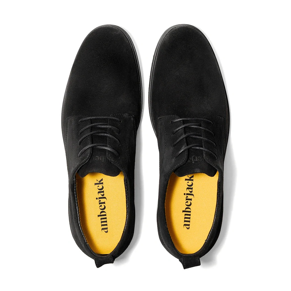 Black suede shoes with yellow soles on a white background