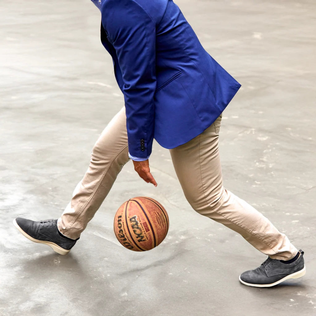 Person dribbling a basketball wearing a blue jacket and beige pants on a concrete floor.