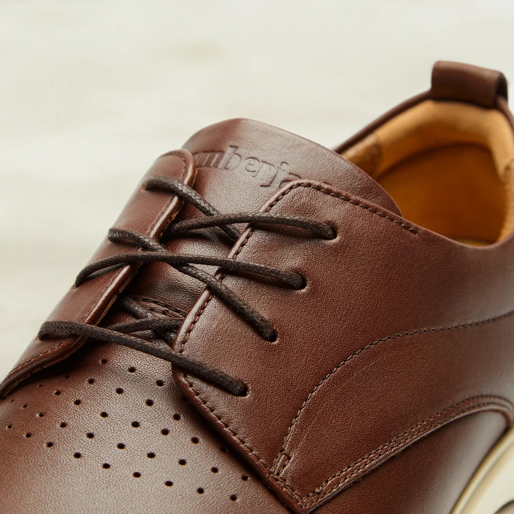 Brown leather shoe with black laces on a beige background