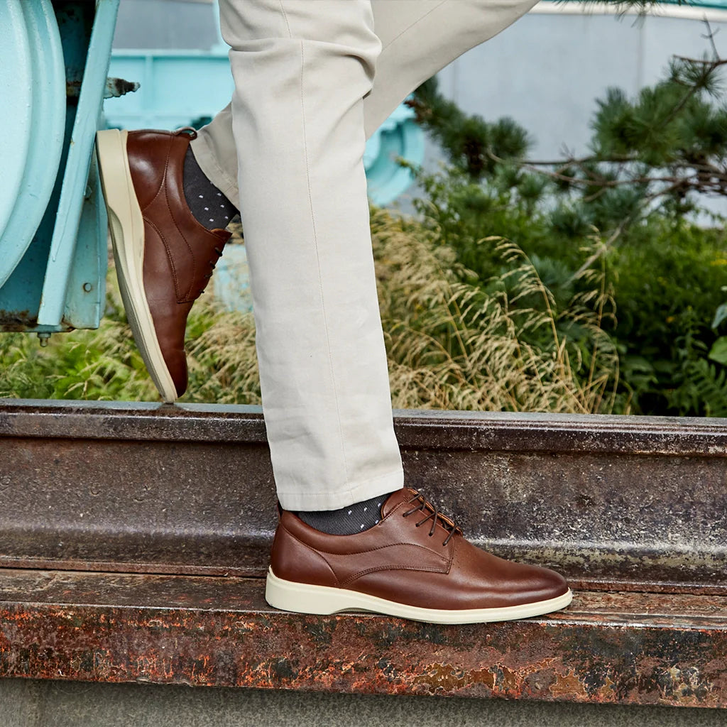Brown leather shoes worn with beige pants on a rustic metal surface.