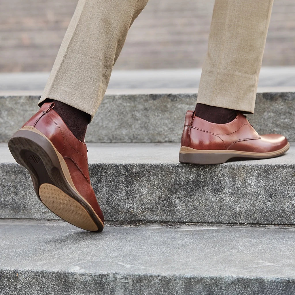 Brown leather shoes worn by a person stepping onto concrete steps.