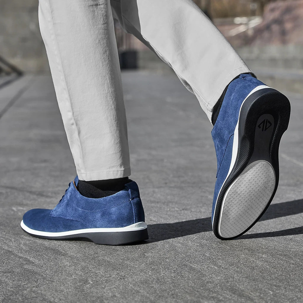 Blue casual shoes worn with light gray pants on a pavement.