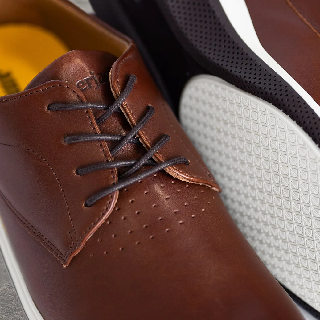 Brown leather shoe with black laces and white sole on a gray surface