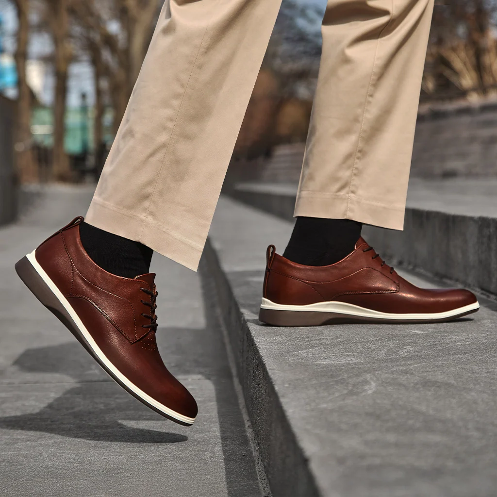 Brown leather shoes with white soles worn by a person on a sidewalk.