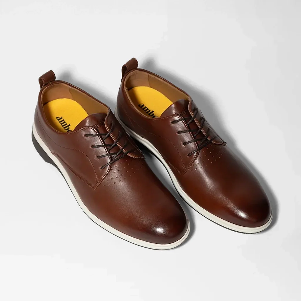 Pair of brown leather shoes with yellow soles on a light gray background