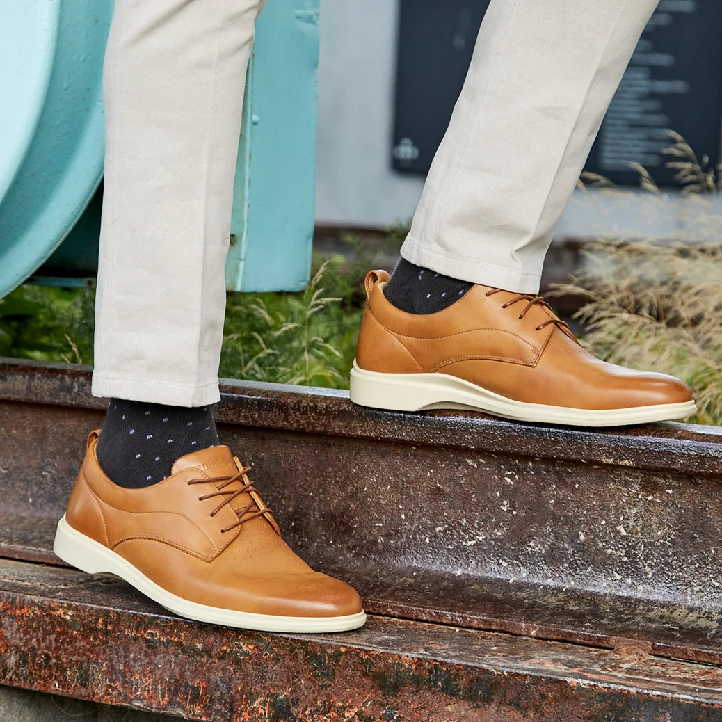 Brown leather shoes worn by a person on metal steps with grass in the background