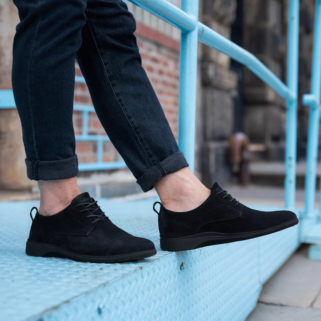 Person wearing black suede shoes standing on a blue platform with blurred background