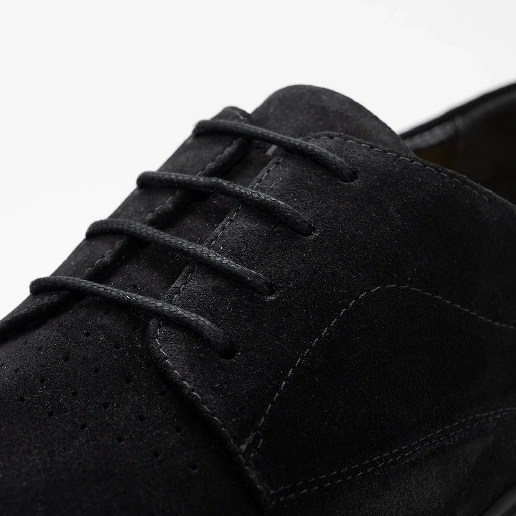 Close-up of a black suede shoe with laces on a light gray background