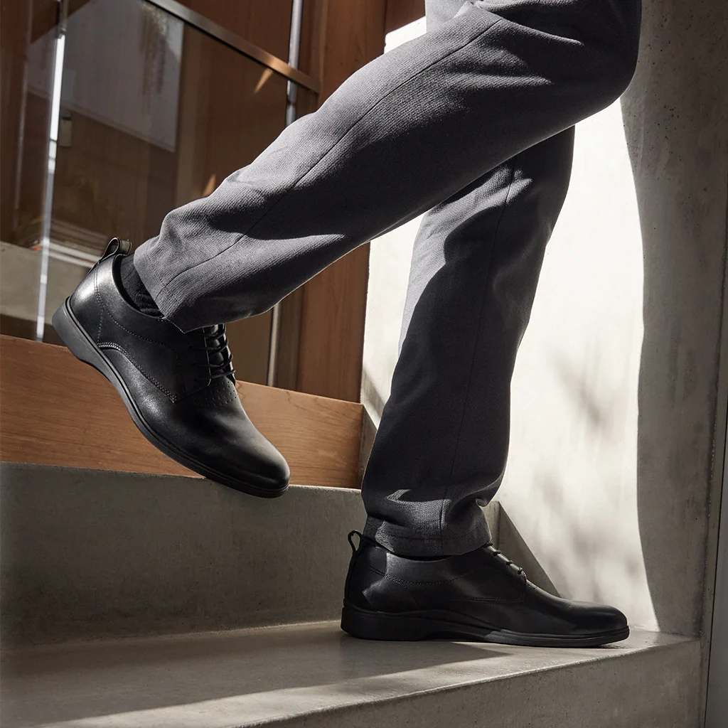 Person wearing black leather shoes and gray pants standing on a staircase.