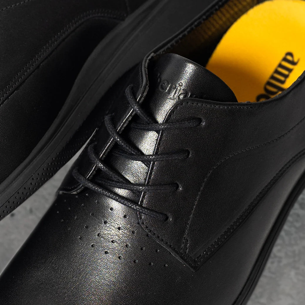 Close-up of a black leather shoe with a yellow sock peeking out, on a gray surface.