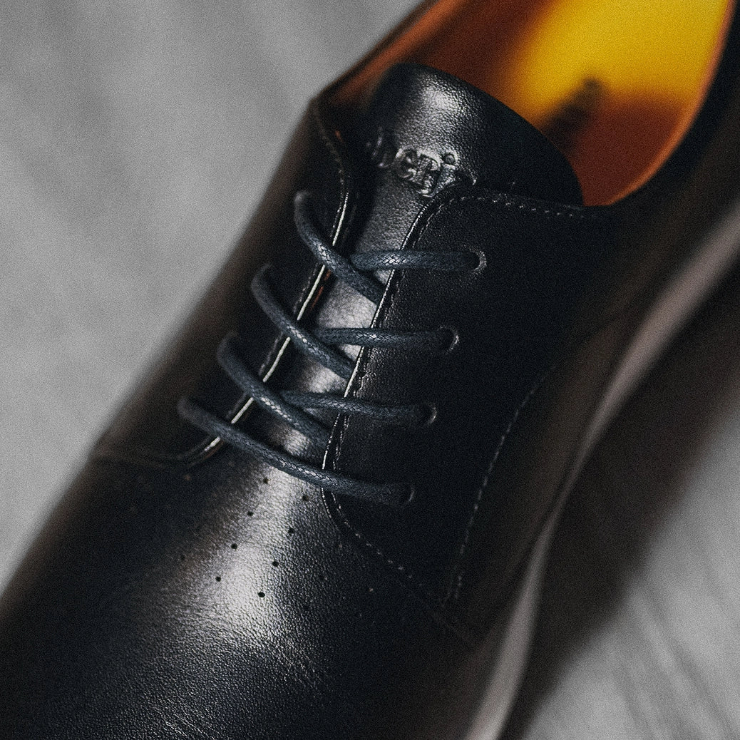 Close-up of a black leather dress shoe with laces on a textured surface.