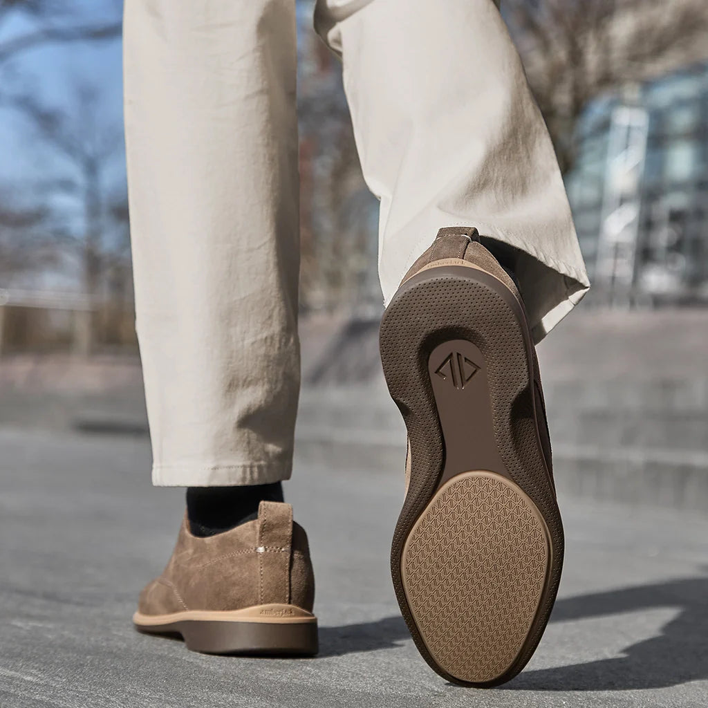 Brown shoes worn with light-colored pants on a blurred outdoor background
