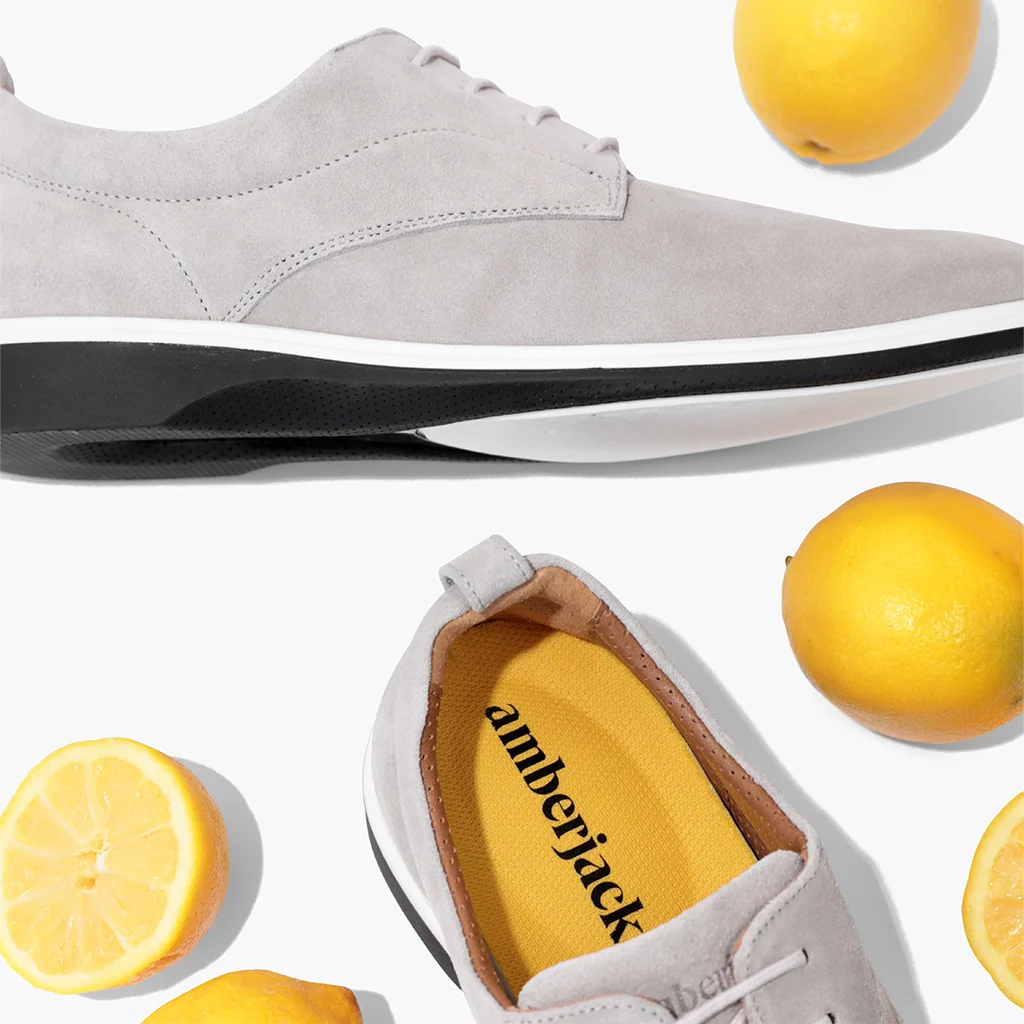 Gray suede shoe with black sole, yellow interior label, and lemons on a white background