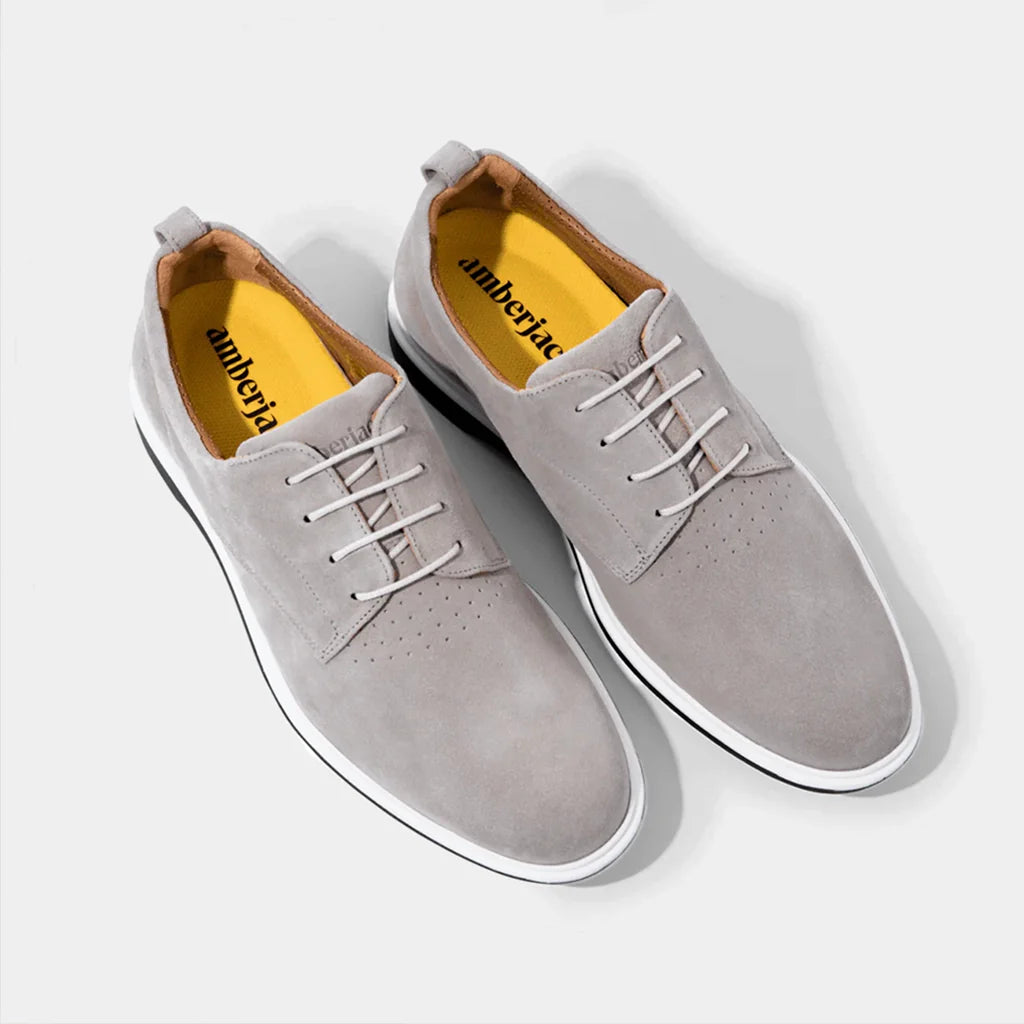 Pair of gray suede shoes with white laces on a light gray background