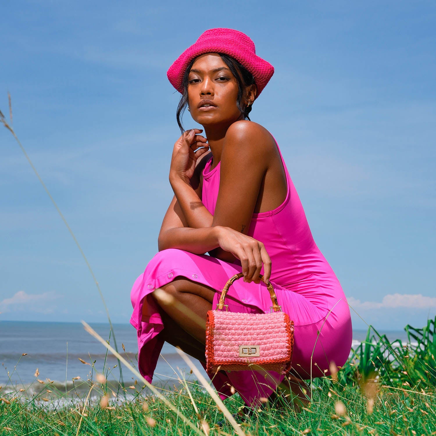 Woman in a pink dress and hat sitting on grass by the ocean
