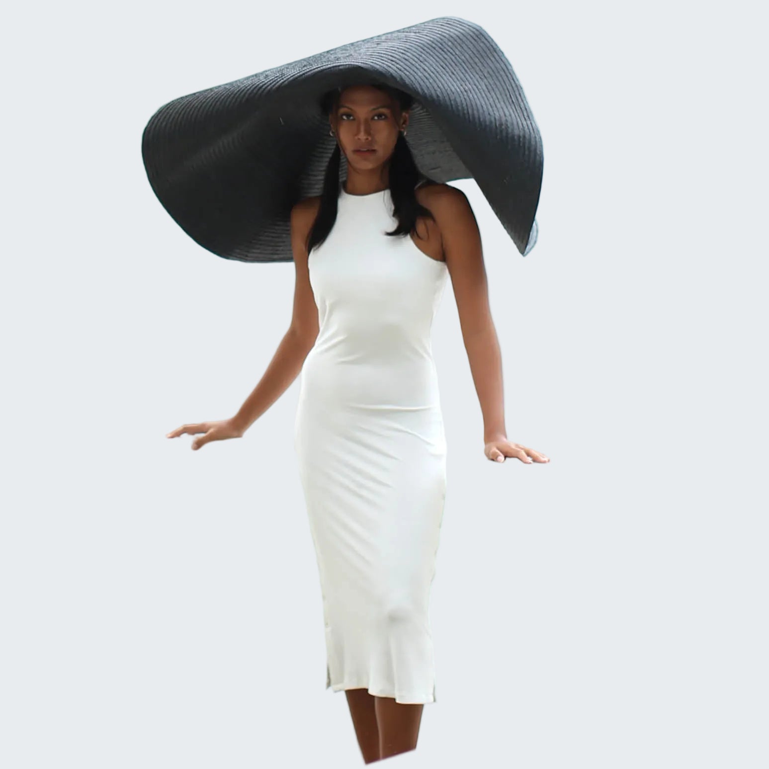 Woman in a white dress with a large black hat standing on a white railing.