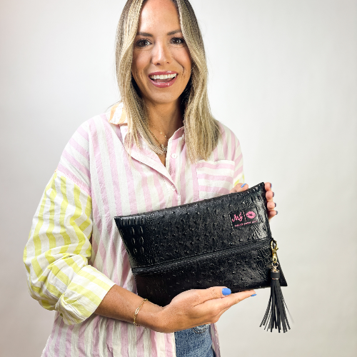 Woman holding a black clutch with a visible brand logo against a plain background