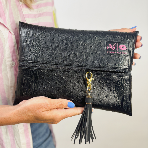 Black textured clutch bag with a tassel held by a person against a neutral background