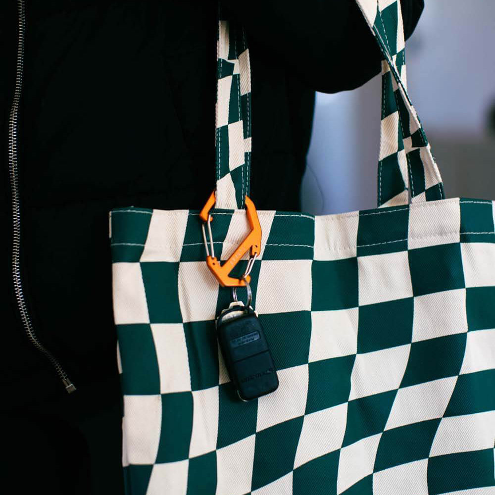 Green and white checkered bag with an orange carabiner and black keychain on a blurred background
