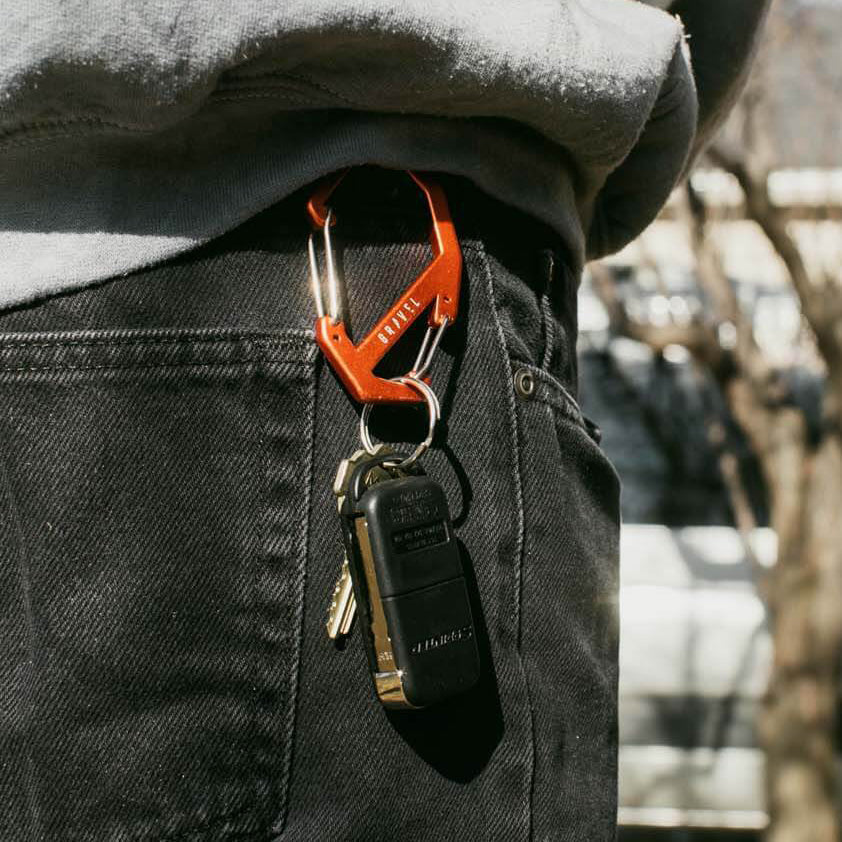 Orange carabiner with keys attached to a person's pocket, blurred outdoor background