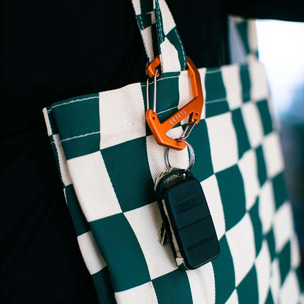 Green and white checkered bag with orange carabiner and black keychain on a blurred background